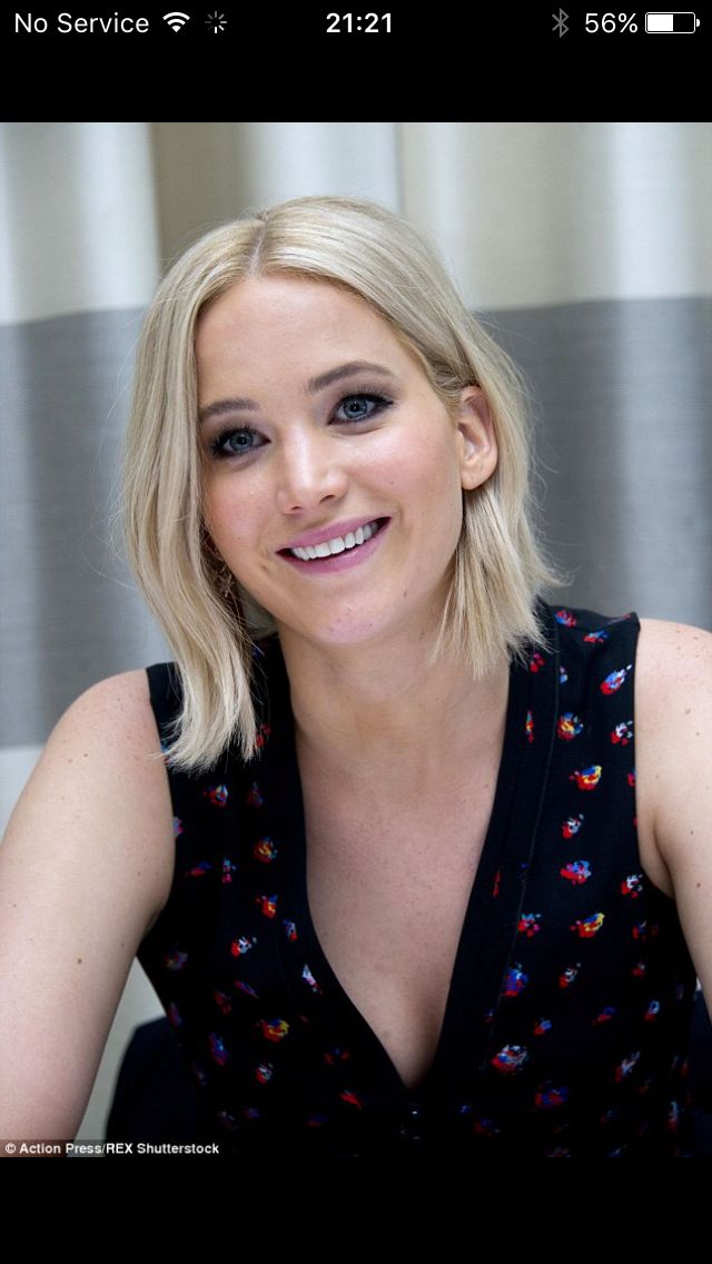 a woman with blonde hair sitting in front of a window smiling at the camera while wearing a black top