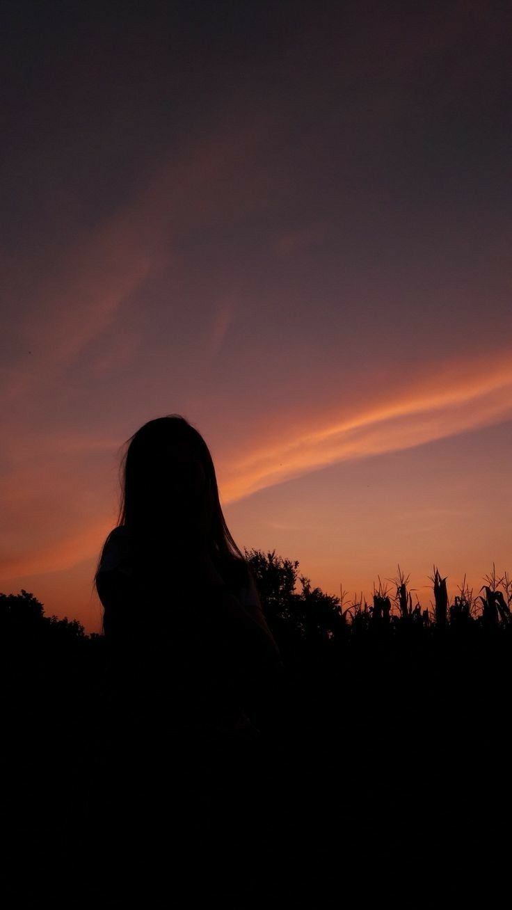 the silhouette of a woman in front of an orange and blue sky at sunset with clouds