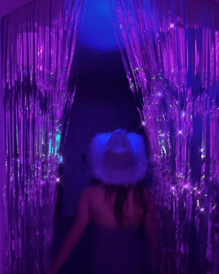 a woman wearing a white hat standing in front of purple curtained walls with lights