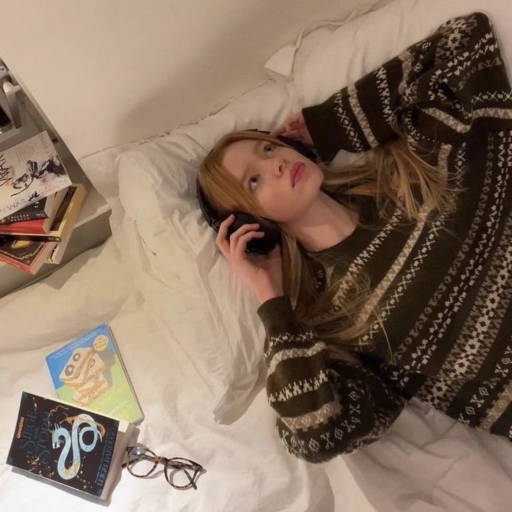 a woman laying in bed talking on a cell phone next to books and eyeglasses