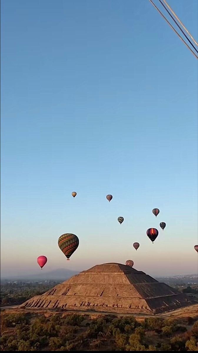 many hot air balloons are flying in the sky over a hill and desert with trees