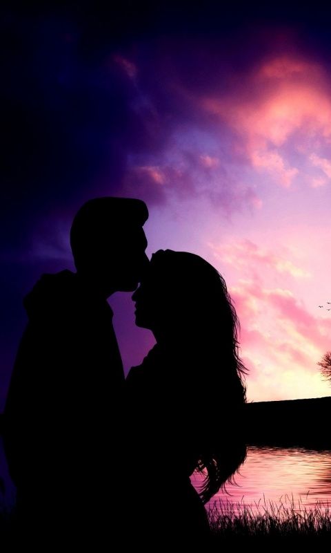 a man and woman standing next to each other in front of a purple sky at sunset