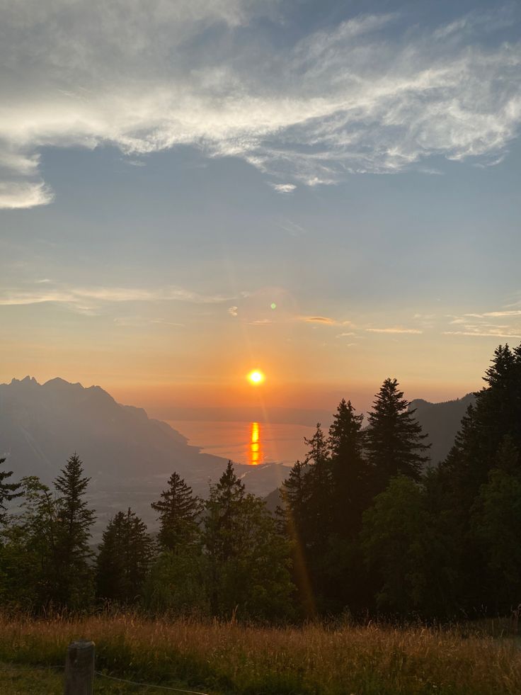 the sun is setting over some mountains and trees