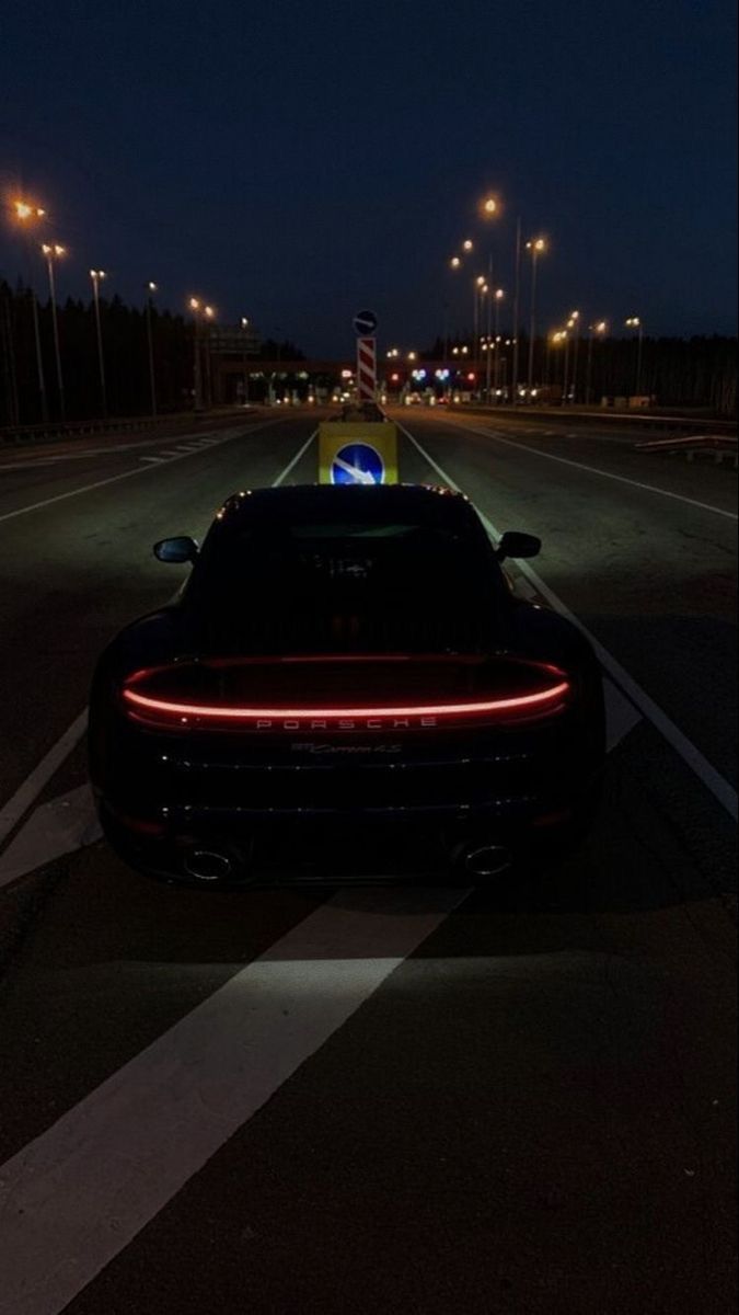 a black sports car is parked on the side of the road at night with its lights on