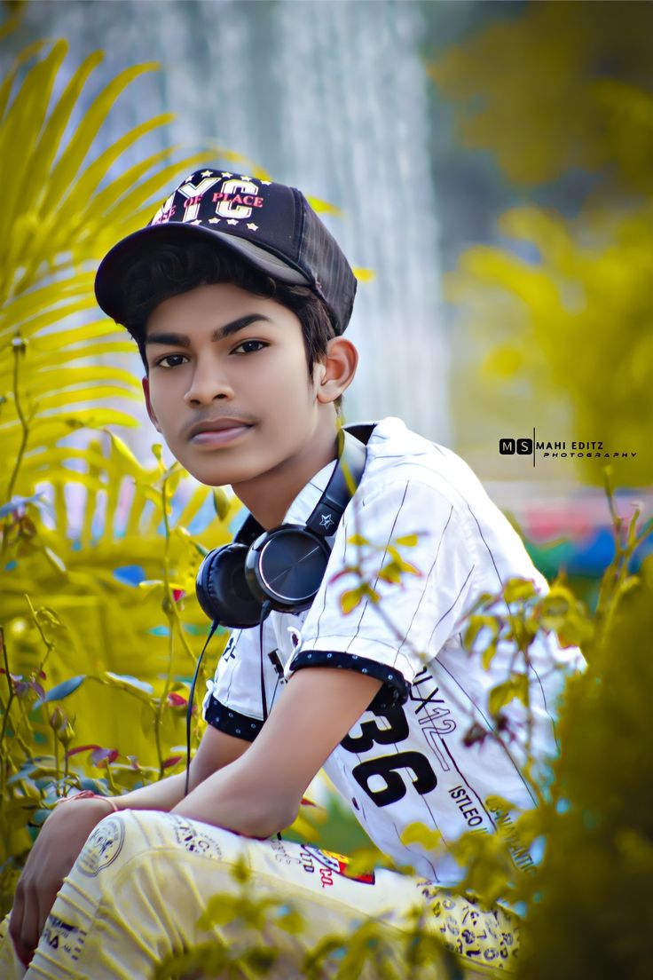 a young boy wearing headphones sitting in front of some plants and flowers with his hands on his hips