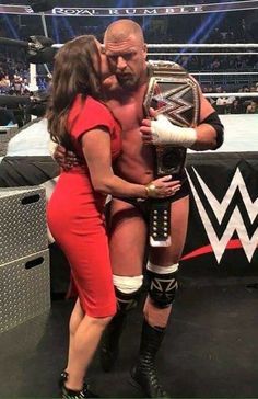 a woman kissing a wrestler on the cheek in front of a wrestling ring at an event