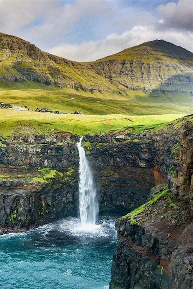 the waterfall is surrounded by green mountains and blue water