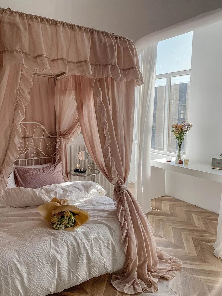 a pink canopy bed in a bedroom with white walls and wood flooring on the side