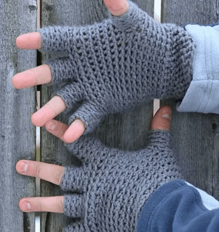 two hands wearing gray knitted gloves on top of a wooden fence