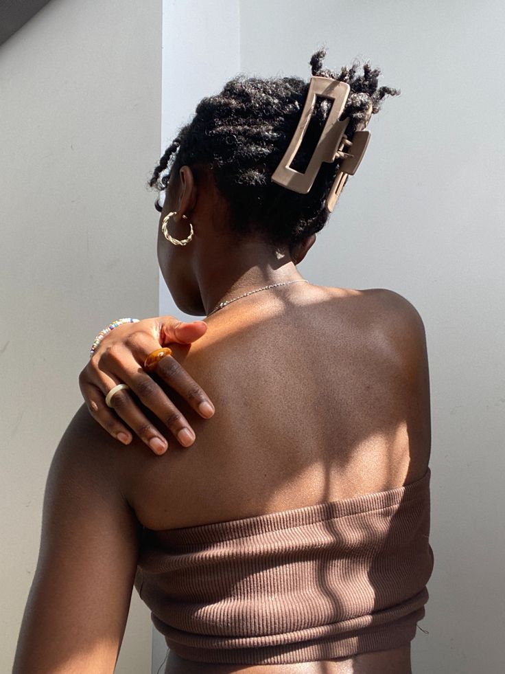 a woman with her back turned to the camera, wearing a brown top and gold rings