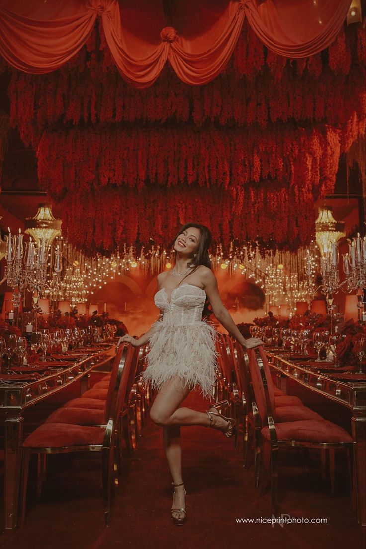 a woman in a white dress posing for a photo with chandeliers hanging from the ceiling