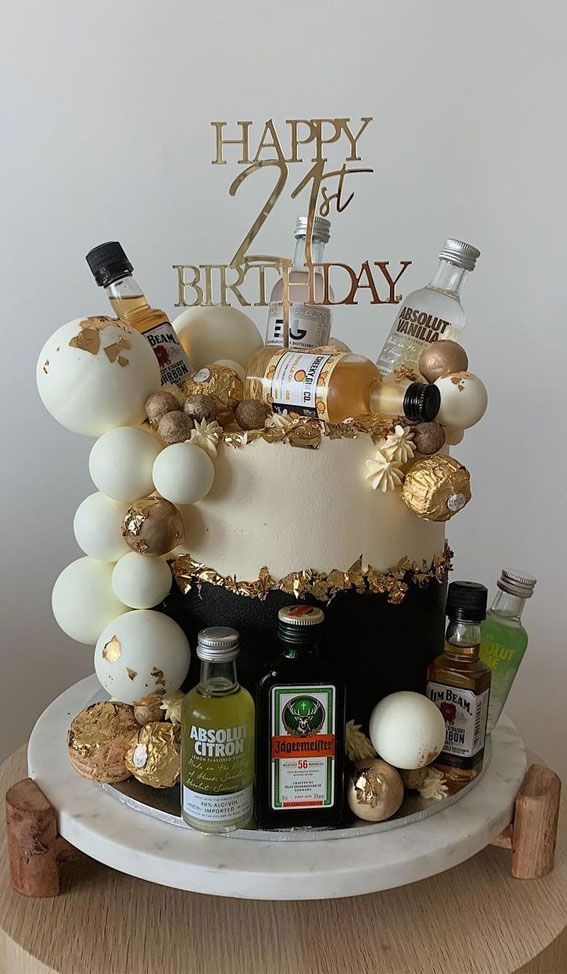 a birthday cake is decorated with gold and white confetti, liquor bottles, and balloons