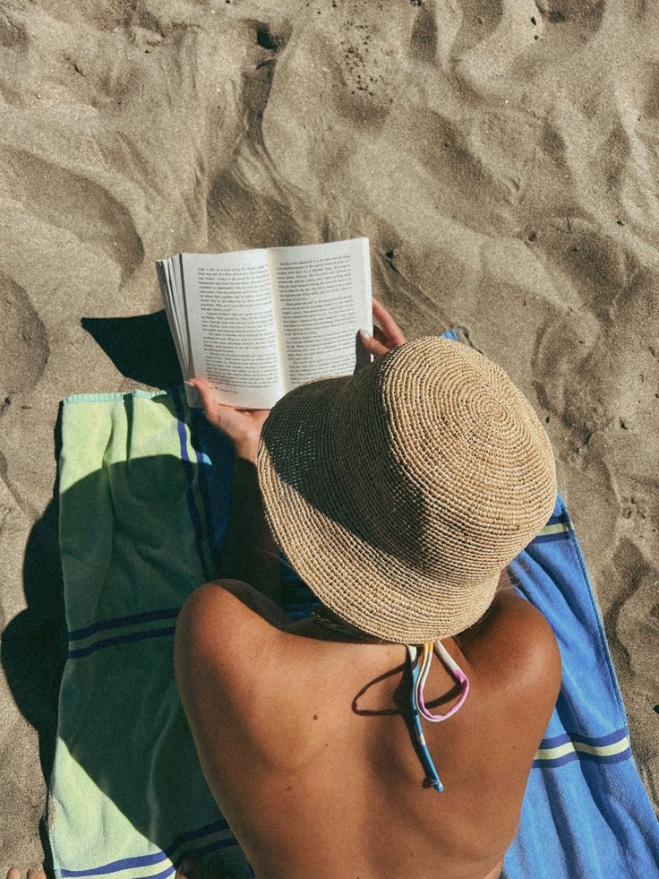 a woman sitting on top of a towel next to an open book in her hand