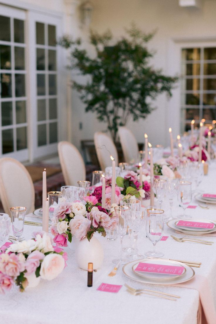 a long table is set with pink and white flowers, candles, and place settings