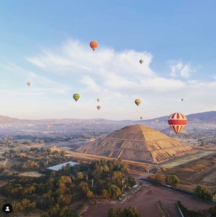 many hot air balloons flying in the sky over a large pyramid and other landforms