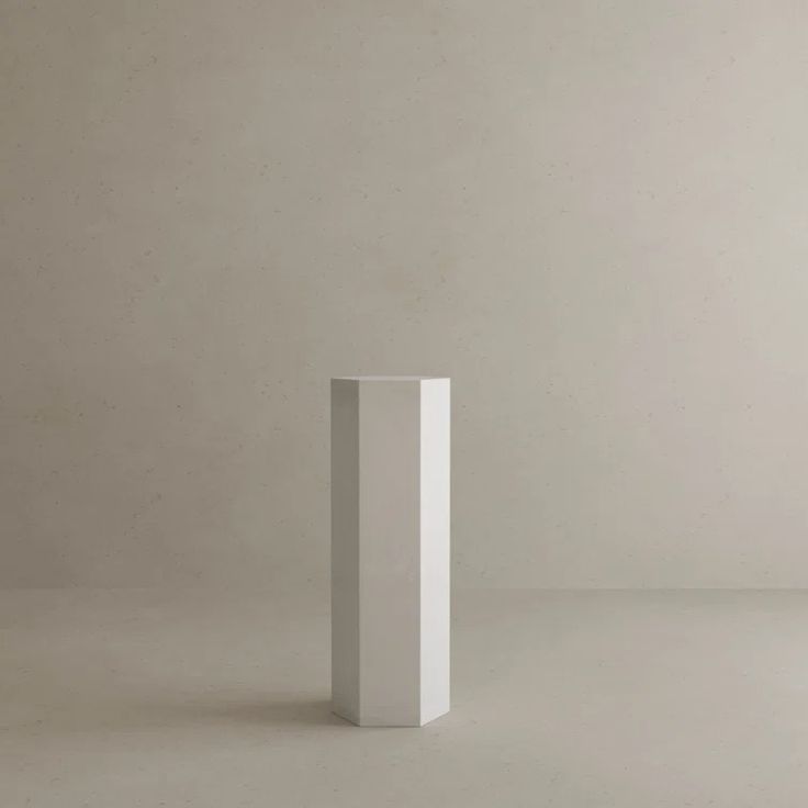 a tall white vase sitting in the middle of a plain room with concrete walls and flooring