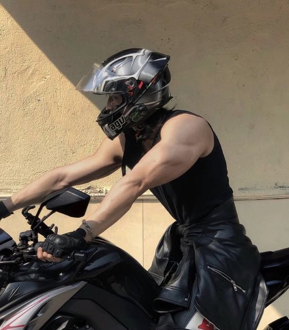 a man wearing a helmet and leather pants sitting on a motorbike in front of a building