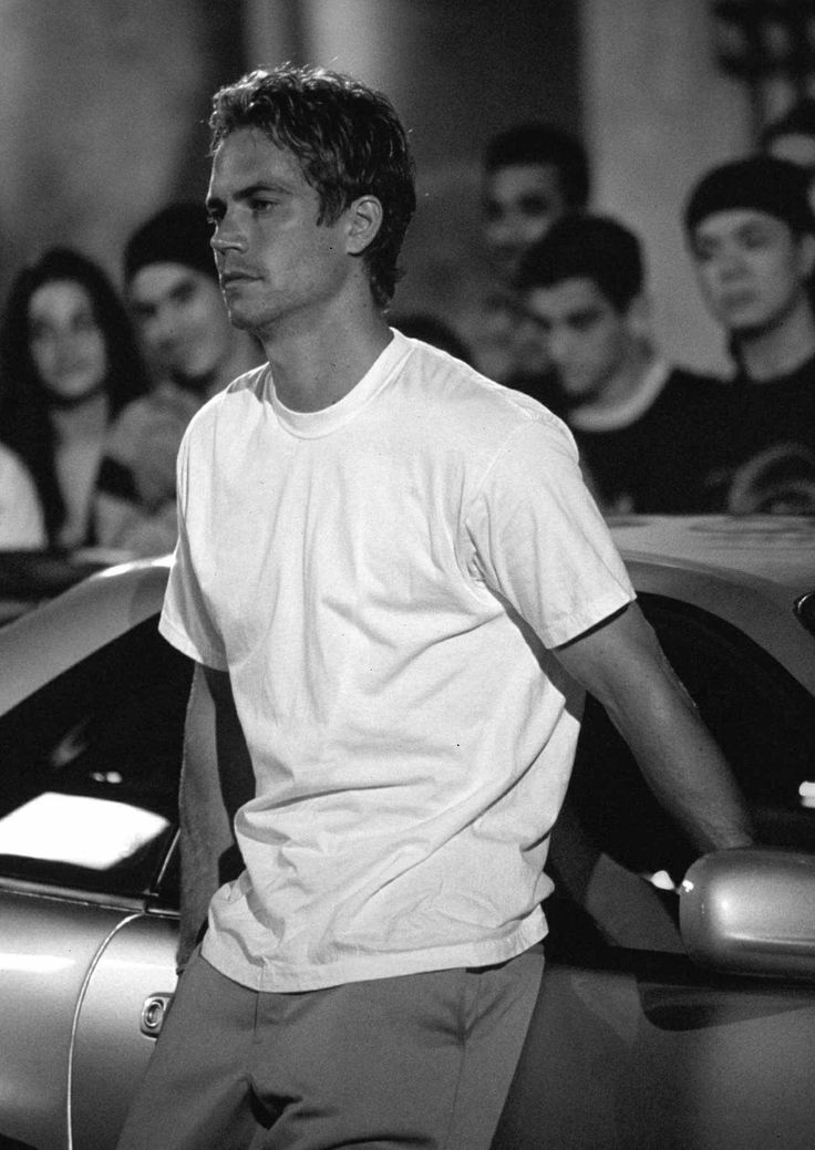 a man standing in front of a group of people next to a blue sports car