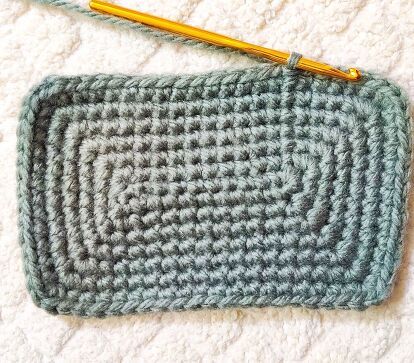 a crocheted gray and white purse with a yellow handled knitting needle on it