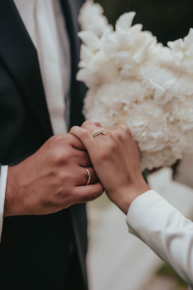 the bride and groom are holding hands with their wedding rings on their fingers while they hold each other's hand
