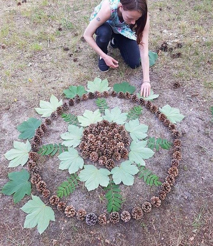 a woman kneeling down in front of a circle made out of pine cones and leaves