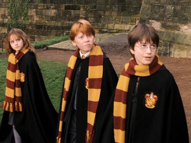 three children dressed in harry potter robes and scarves, walking down the street together
