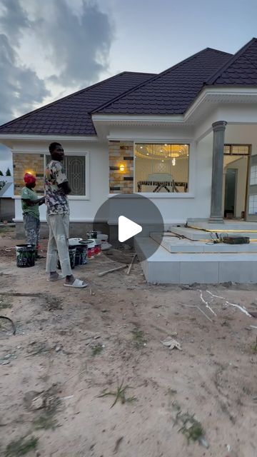 two men standing in front of a house under construction with tools on the ground and one man holding a bucket