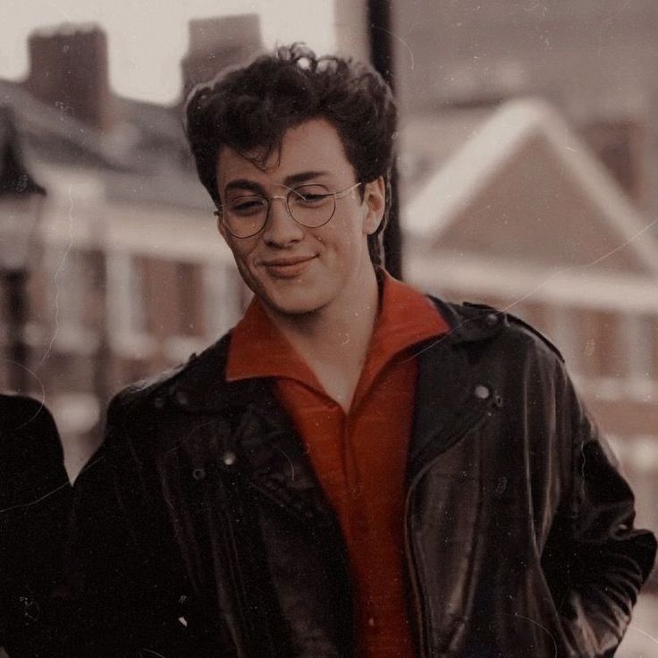 a man wearing glasses and a leather jacket is looking at his cell phone while standing in the street