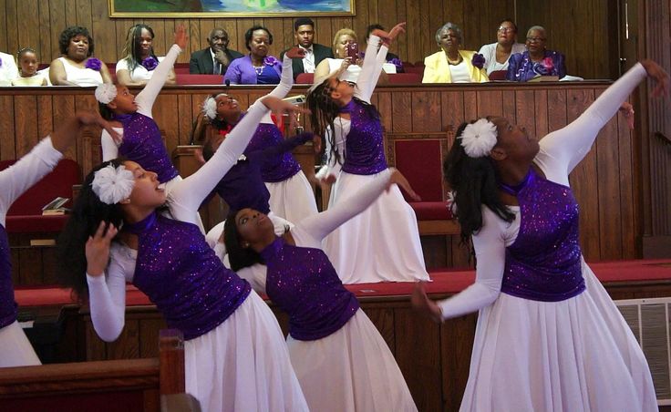 several women in white and purple dresses are dancing on stage with their hands up to the ceiling