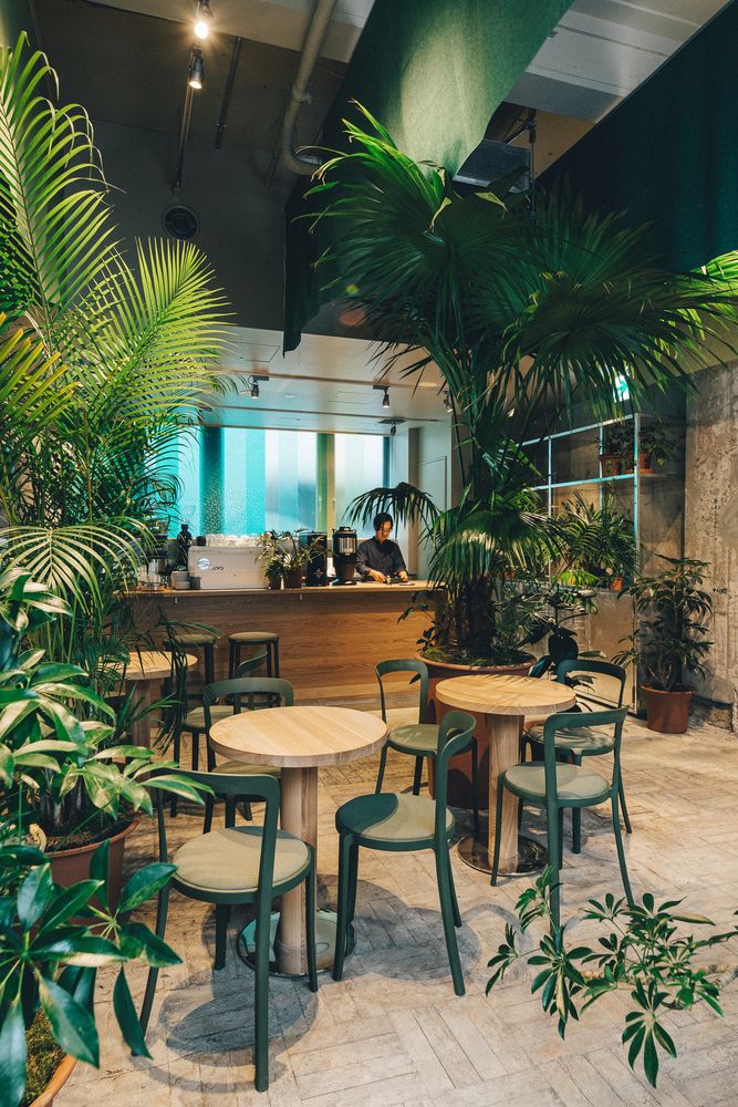 an indoor cafe with tables and chairs surrounded by potted plants