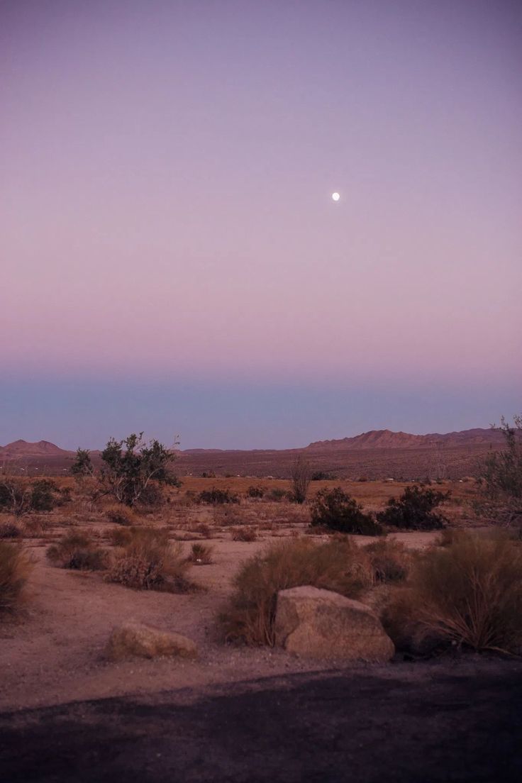 the moon is setting in the sky over some desert