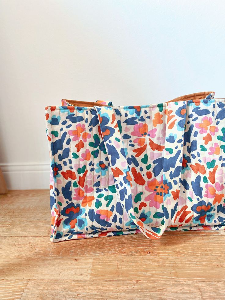 a multicolored floral print bag sitting on top of a wooden floor next to a white wall