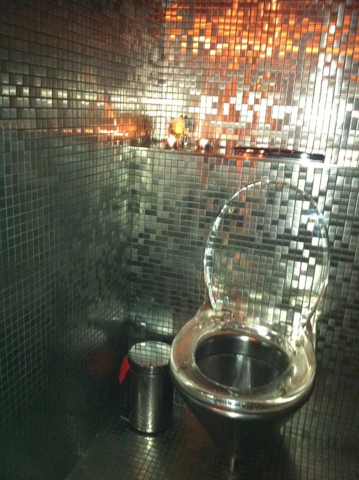 a bathroom with a shiny toilet and chrome sink in the corner, next to a trash can