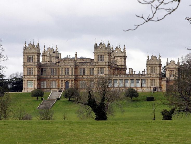 a large building with many windows on top of a green hill in front of trees