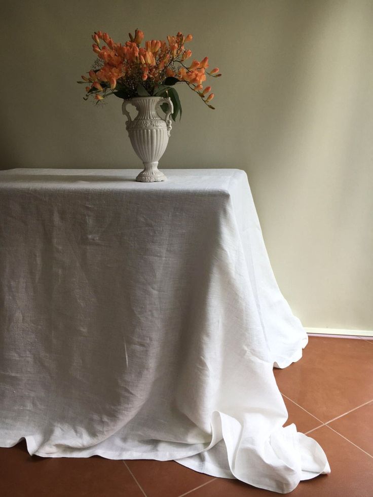 a white vase with orange flowers sitting on top of a table covered in a white cloth