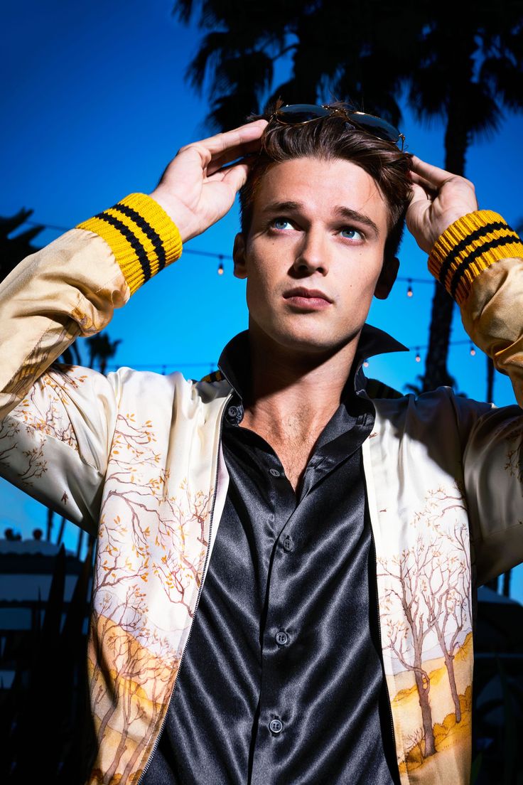 a young man is holding his hands to his head and looking at the camera while standing in front of palm trees