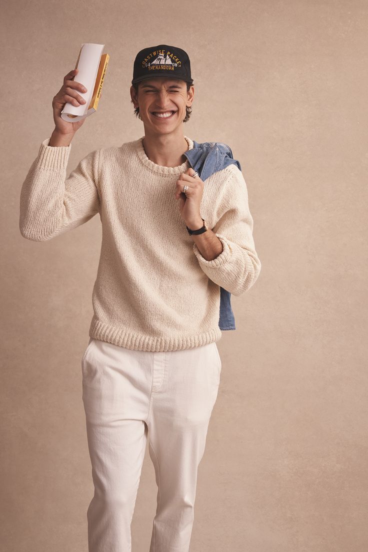 a young man is smiling and holding something up to his face while standing in front of a beige background