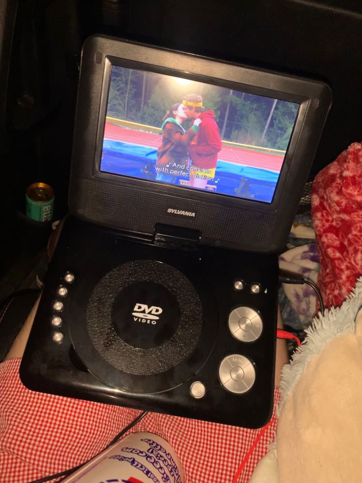 an open dvd player sitting on top of a bed next to a teddy bear and bottle