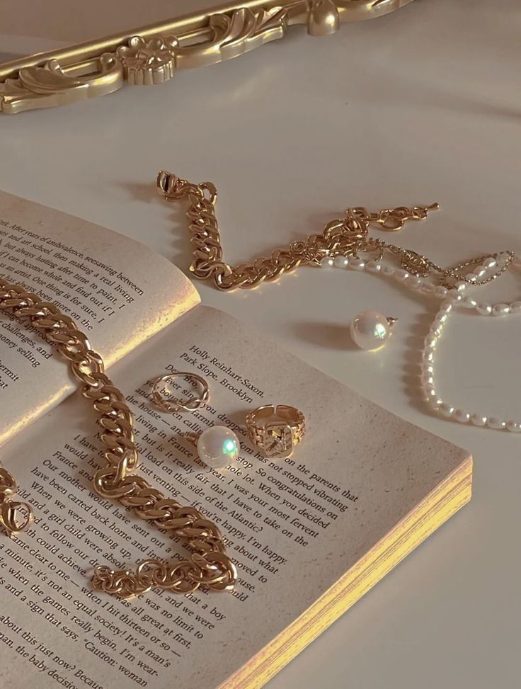 an open book with gold jewelry on it next to a chain, bracelet and ring