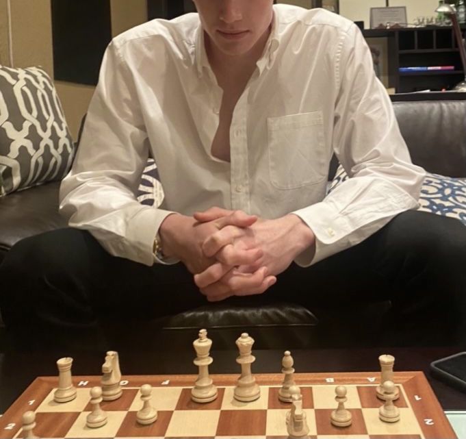 a man sitting on a couch with his hands folded over the chess board while looking at the camera