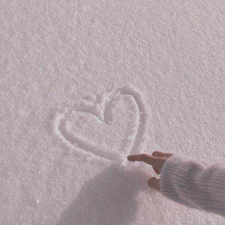 a person's hand is touching the snow with a heart drawn on it