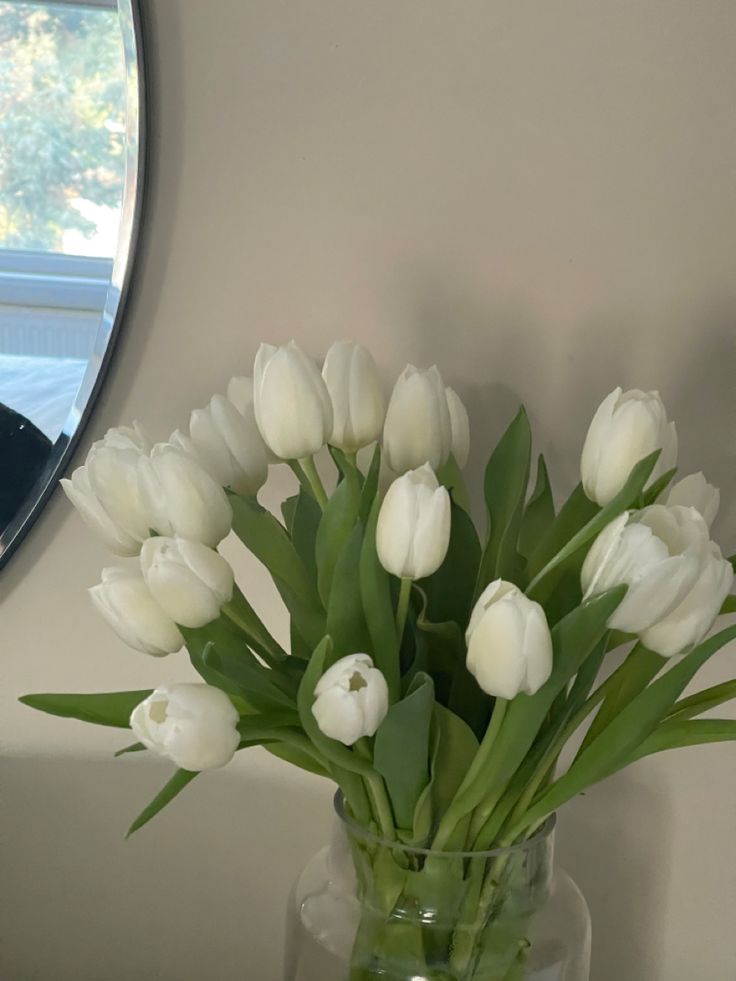 a vase filled with white tulips sitting on top of a table next to a mirror