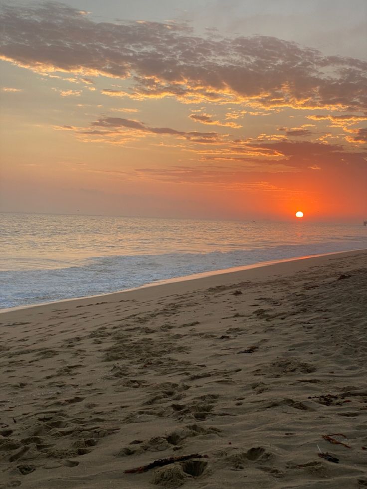 the sun is setting at the beach with footprints in the sand