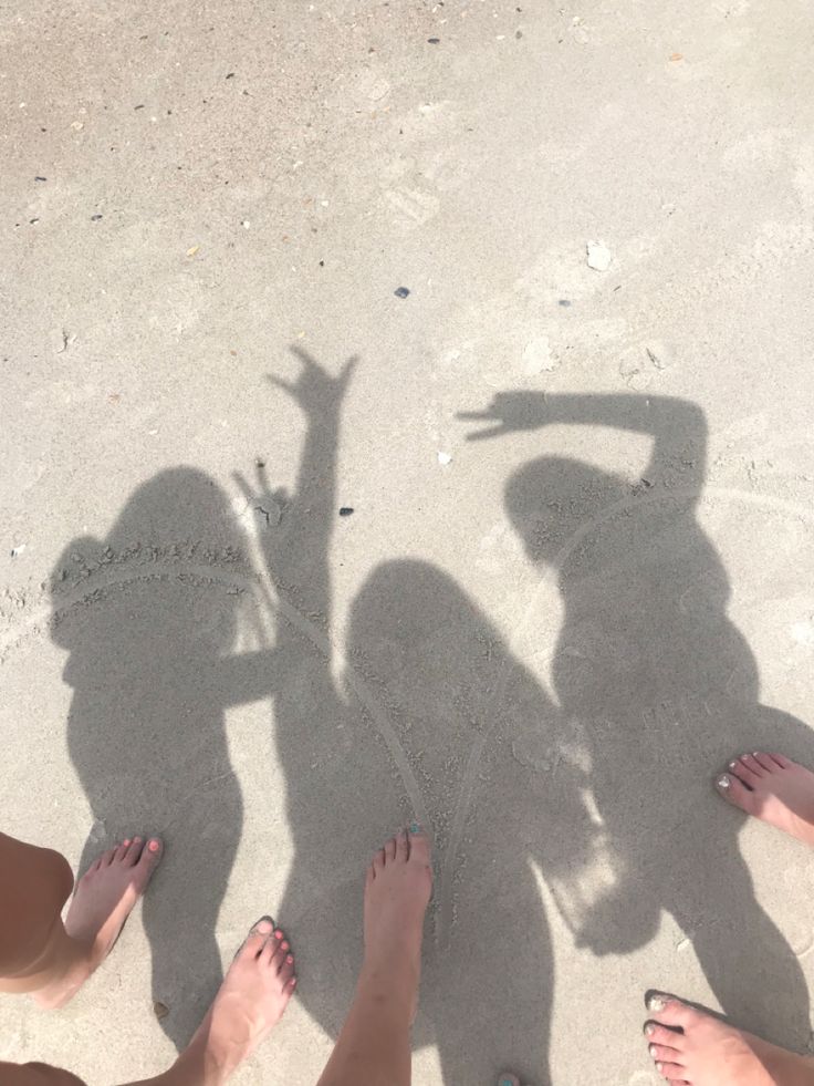 four people are standing in the sand with their shadows on the beach and one person is holding her hand up