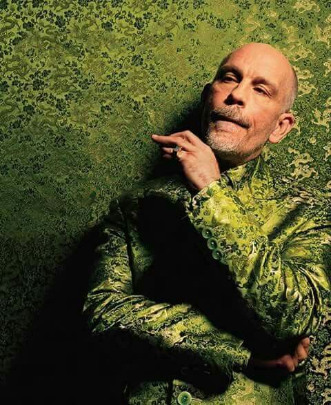 a man in a green suit leaning against a wall with his hand on his chin