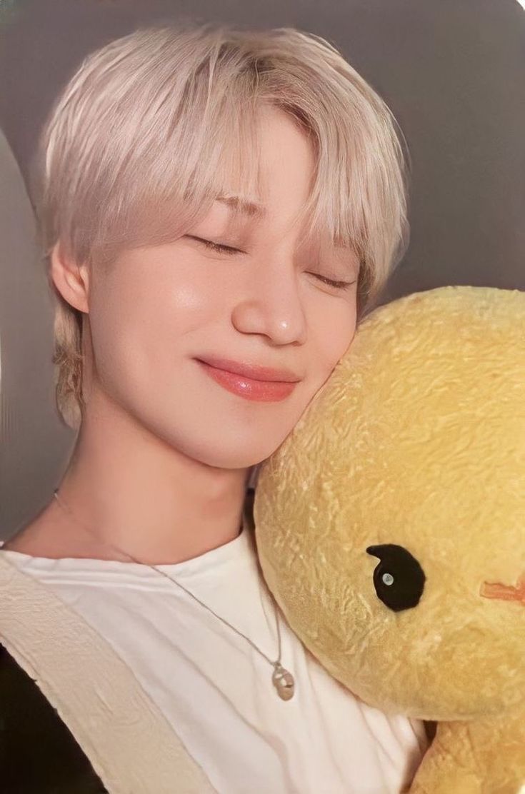 a person holding a yellow teddy bear in their arms and smiling at the camera with eyes closed
