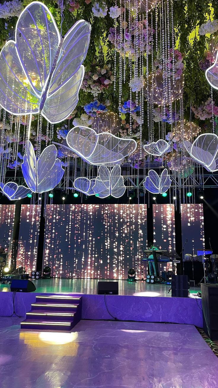 an indoor dance floor with purple lighting and flowers hanging from it's ceiling above