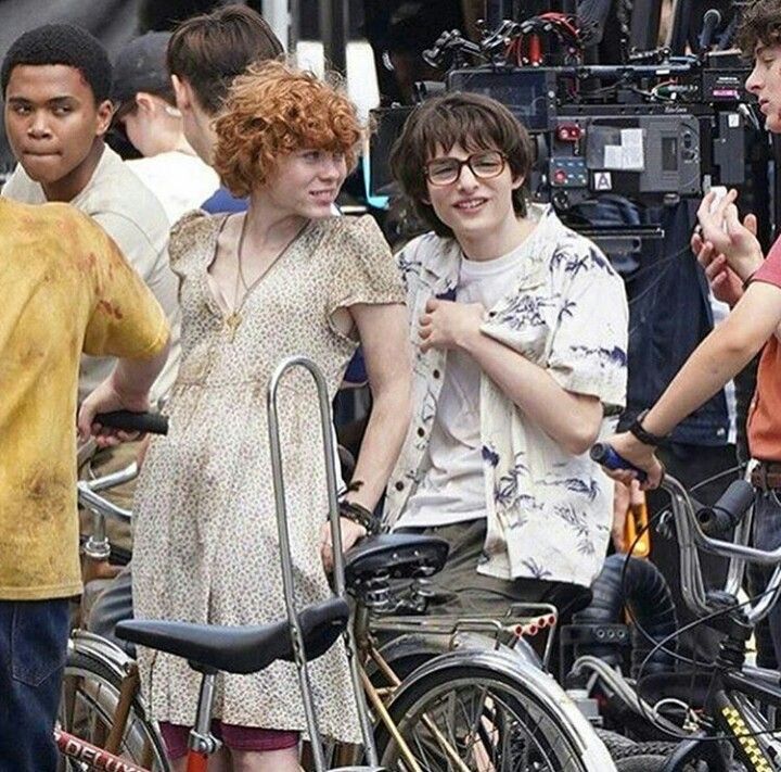 the young people are standing around with their bikes in front of them and behind them is a cameraman