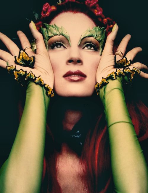 a woman with red hair and green make - up holding her hands to her face