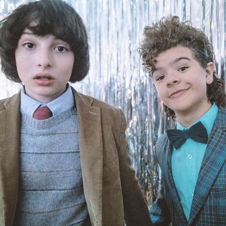 two young boys wearing suits and bow ties standing next to each other in front of a curtain